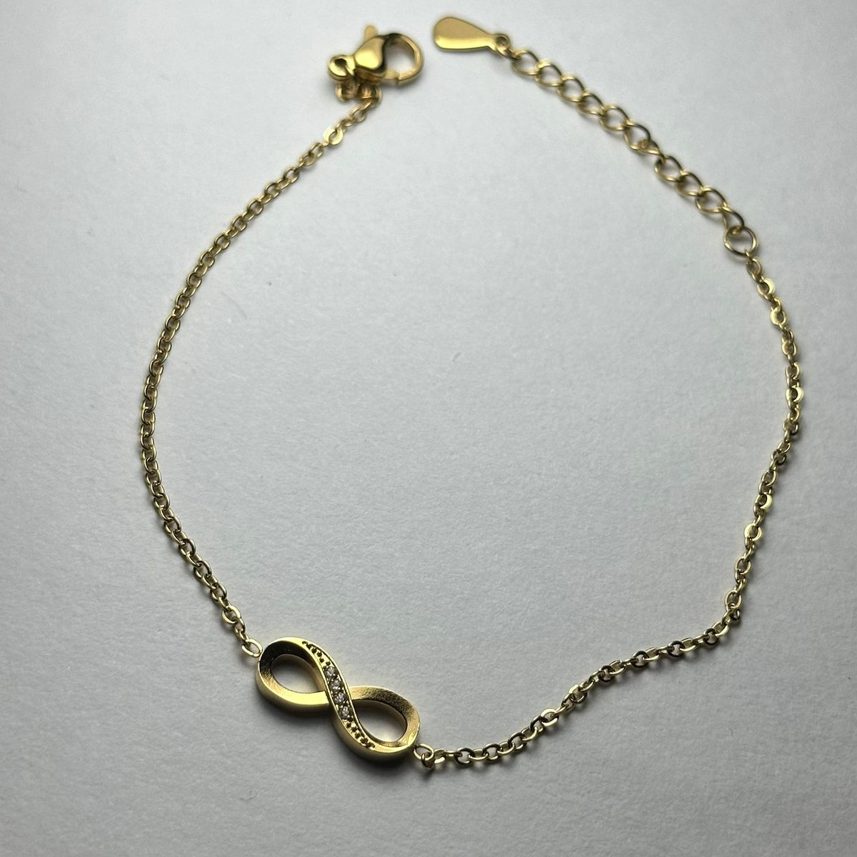 Pulsera simple con infinito en medio y piedras.oro